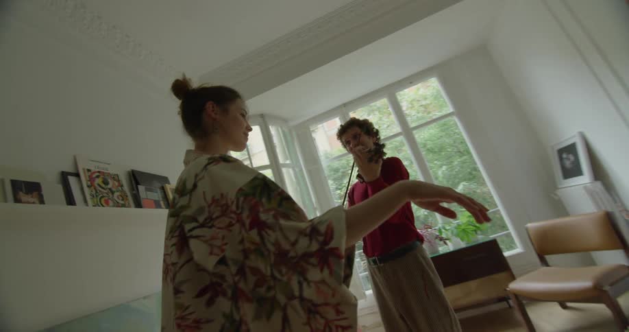 A man playing a violin as a woman dance in a room with a wall and window in the background