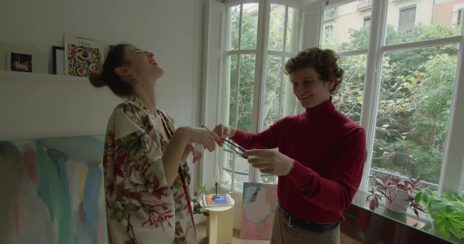 Man teaches woman how to hold violin bow while they stand in room in apartment