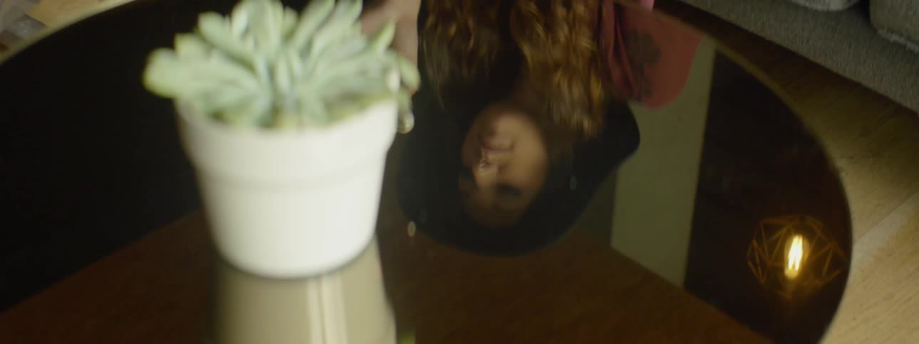 A woman sipping from a coffee cup is reflected in a shiny coffee table