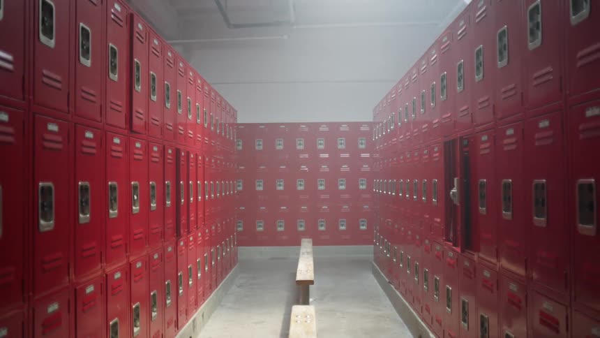 Bench in the middle of a row of red lockers in a locker room