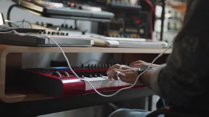 A person in a room sitting on a chair playing a keyboard with a wall in the background
