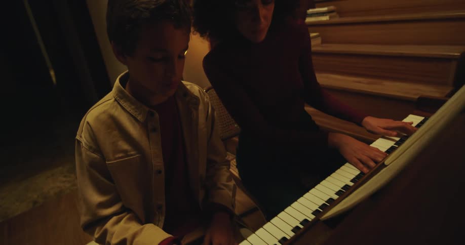 Woman with curly hair teaches youth the piano near steps