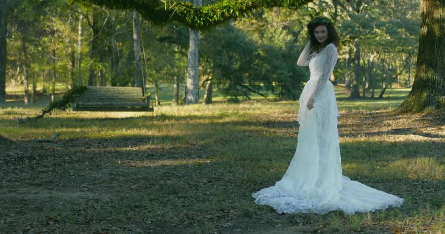 A bride in a white lace gown pushes her hair back and smiles while posing near a swing