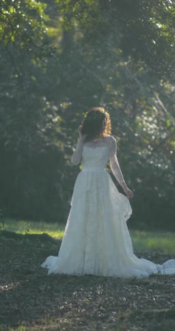 A woman standing outside in a wedding dress with grass and trees in the background