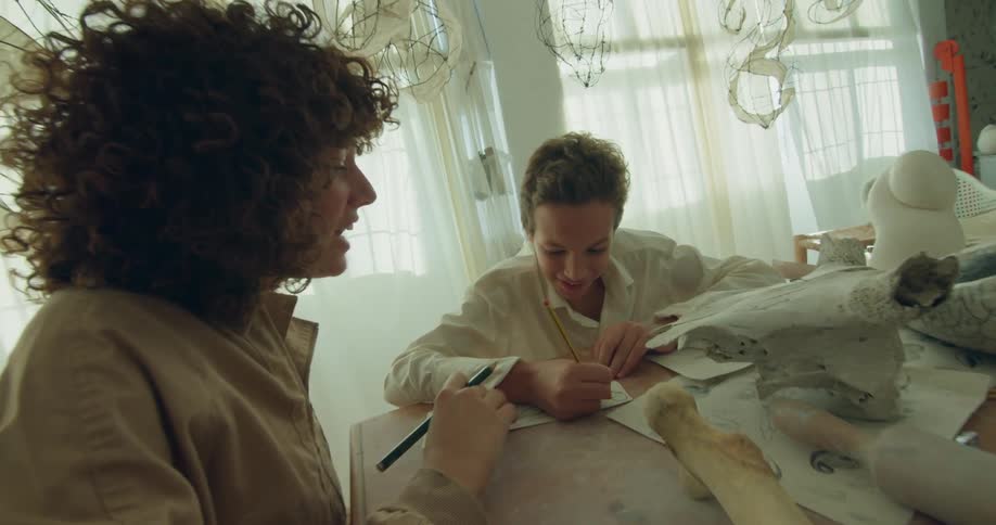 Woman with curly hair giving a young boy lessons inside an artist studio at daytime