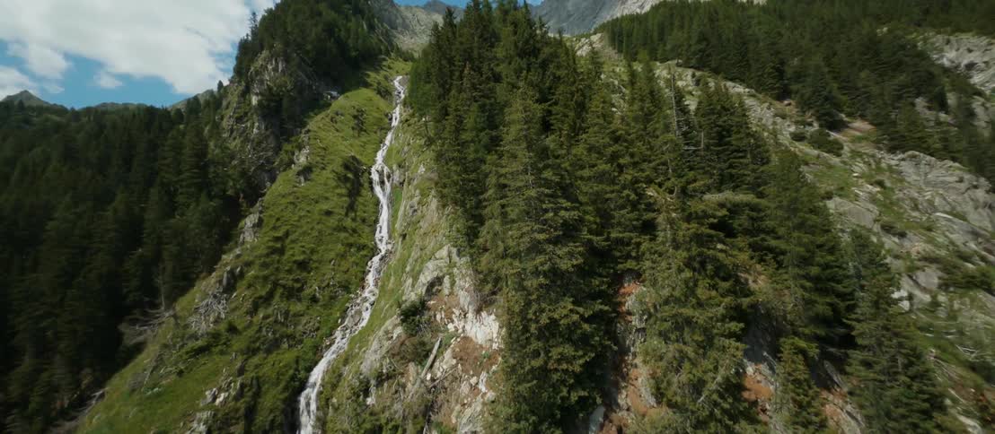 A waterfall down the side of a mountain covered in forest on a sunny day