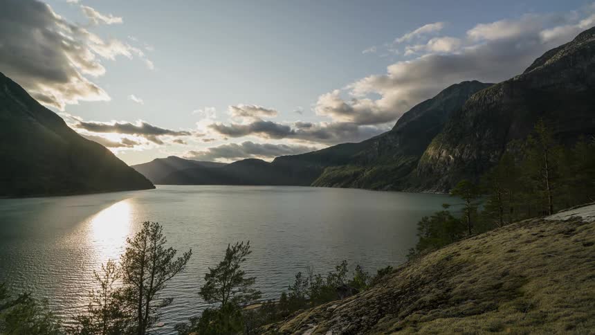 A river with water with a mountain range the sky and clouds in the background