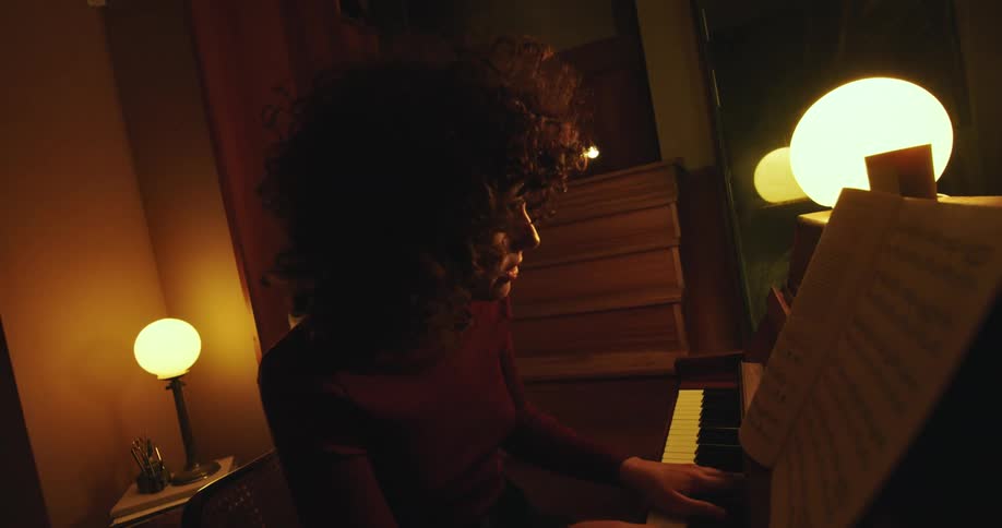 A woman in a room playing a piano with a wall and doorway in the background