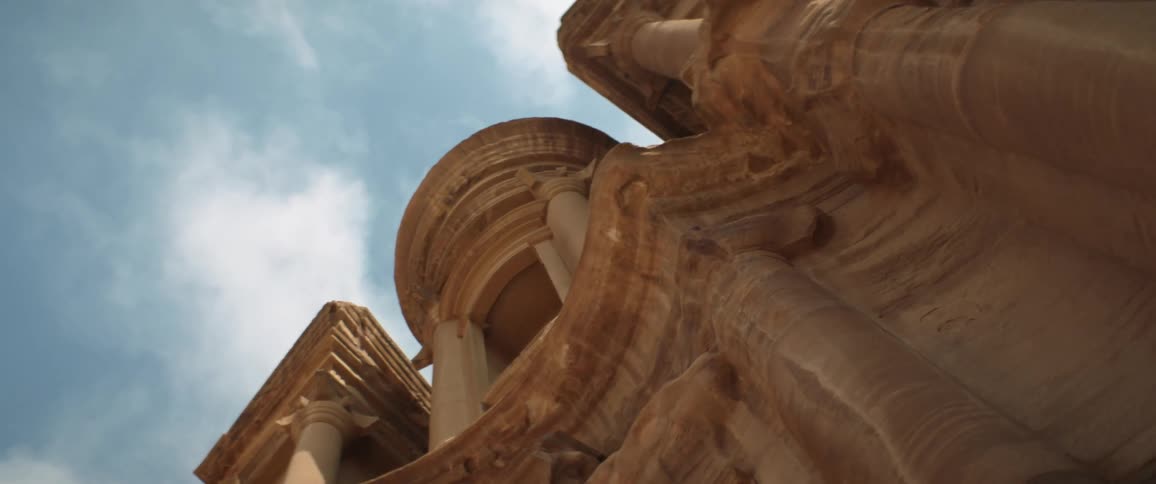 Buildings sculpted from reddish stone stand under cloudy sky