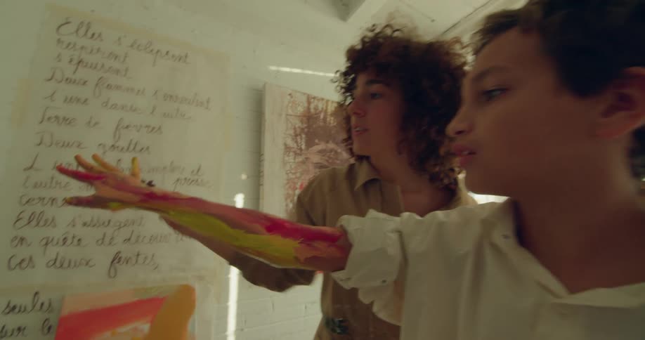 Female painter with brown shirt and curly hair paints boys arm with white polo shirt in the studio