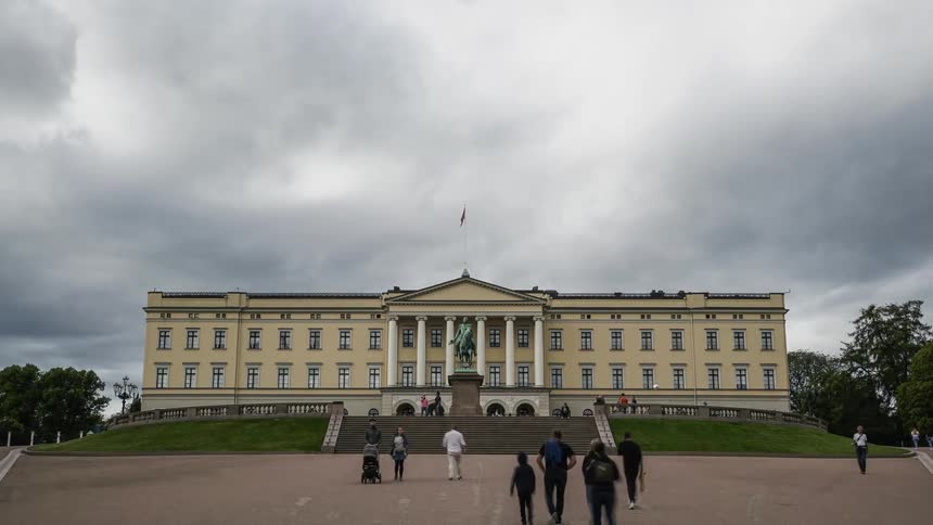 People are walking around oslos royal palace under a cloudy sky