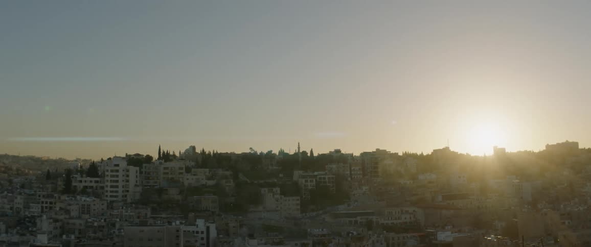 The sun is setting over a hilltop covered with houses and buildings in a city