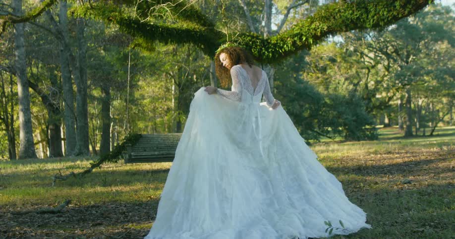 A woman is walking in the woods wearing a long wedding dress