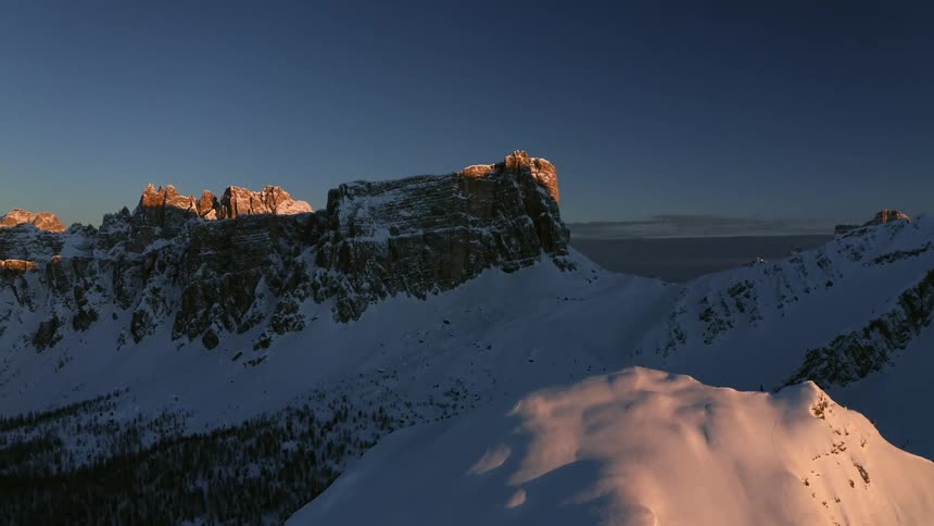 A cliff covered in snow with a mountain range the sky and clouds in the background