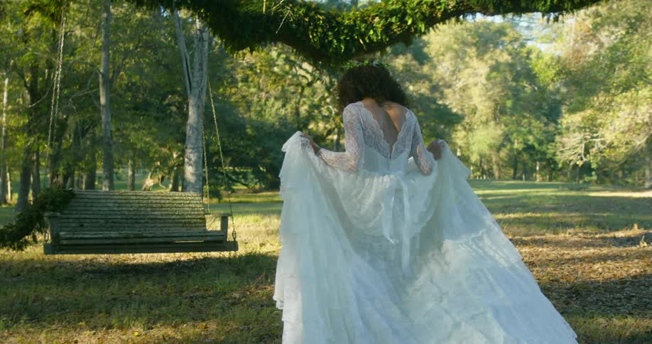 A smiling bride picks up her train and walks toward a swing to pose for pictures
