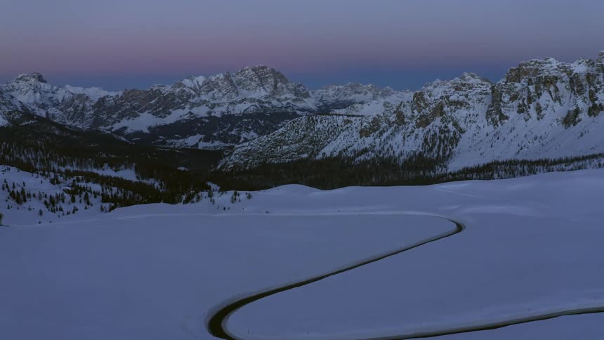 Waterway winds across snow covered plain toward forest and mountains under red tinted sky