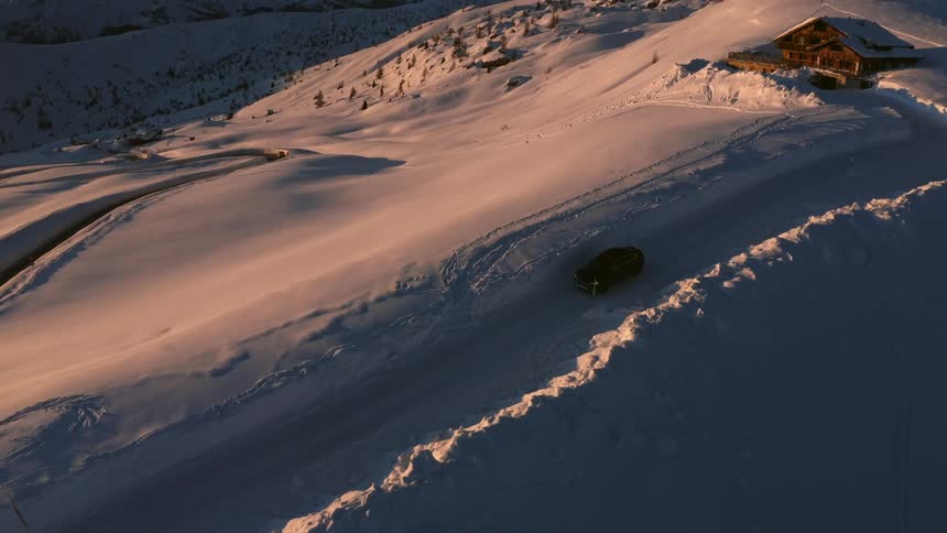 A car travels on a snowy road on the top of a mountain ridge