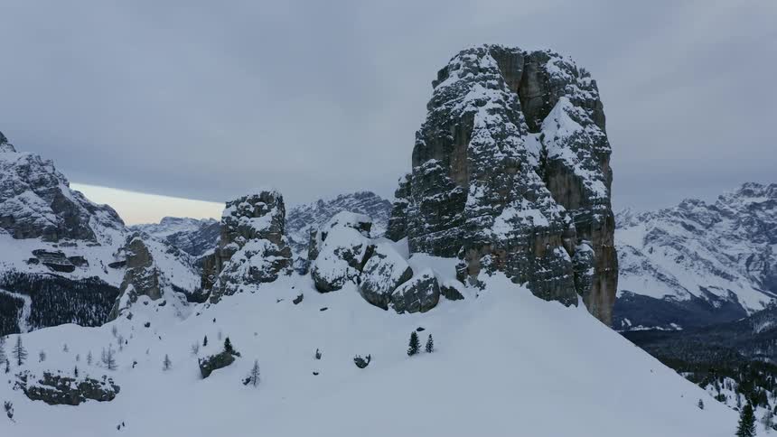 A cliff covered in snow with a mountain range the sky and clouds in the background
