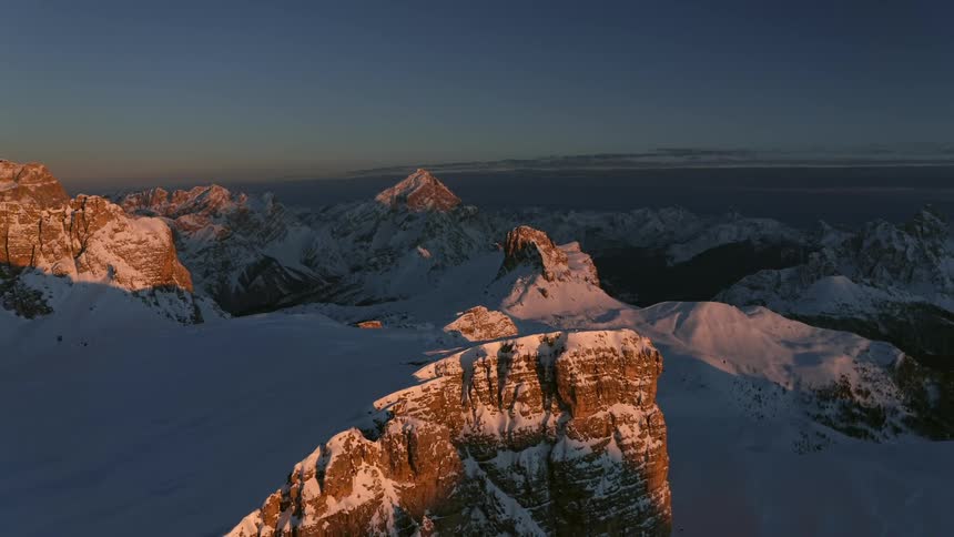 The sunlight shines along the top of a snow covered mountain cliff
