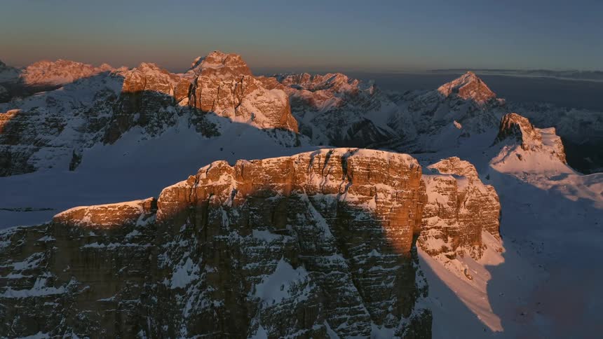 The sun shines on a snow covered mountain ridge