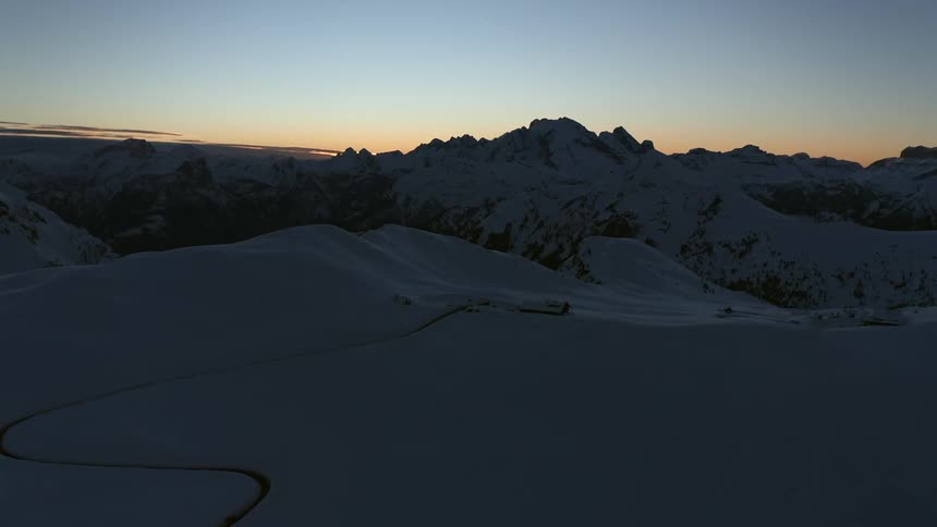 A curvy trail winds through the snow on a mountain range