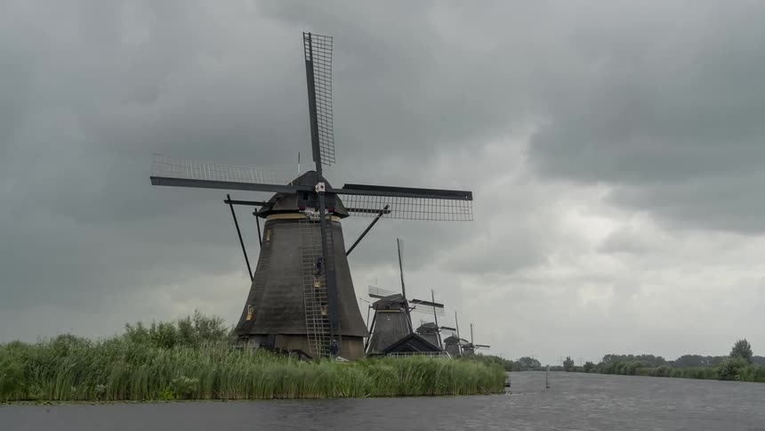 A row of still windmills along a river with gray clouds moving overhead