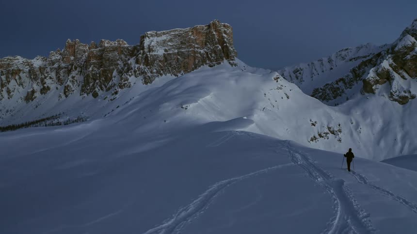 A person is hiking on a snowy mountain top using poles for balance