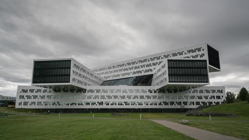 A building with people a walkway and grass in the foreground with the sky and clouds in the background