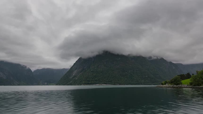 Person rides across waves leaving wake with low lying clouds touching promontory in background