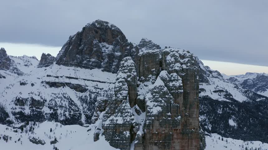 A tall rock formation on the summit of a snowy mountain under a cloudy sky