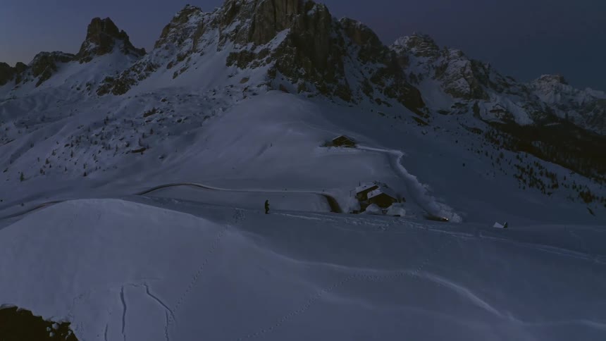 A person walking on a hill with snow with a mountain range the sky and clouds in the background