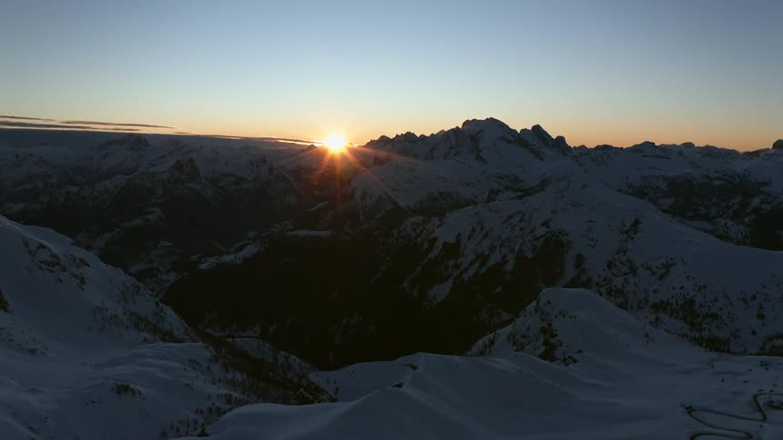 The sun rises on the horizon over a snow covered mountain range