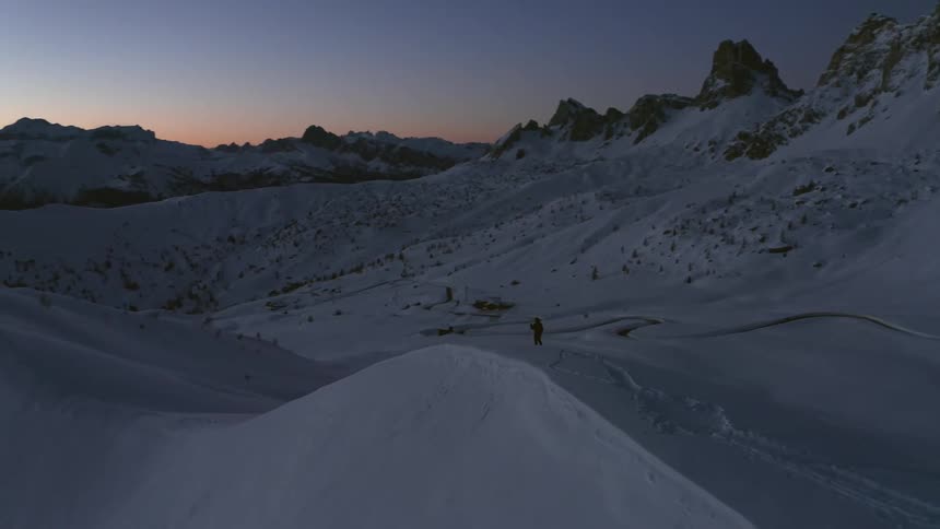 Someone is walking across a snow covered mountain ridge with trekking poles