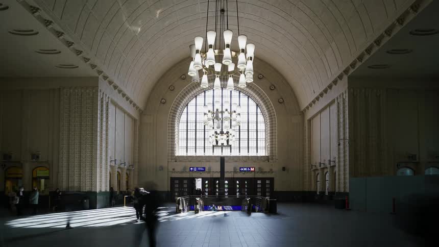 Heavy crowds pass through the open foyer of a train station throughout the day