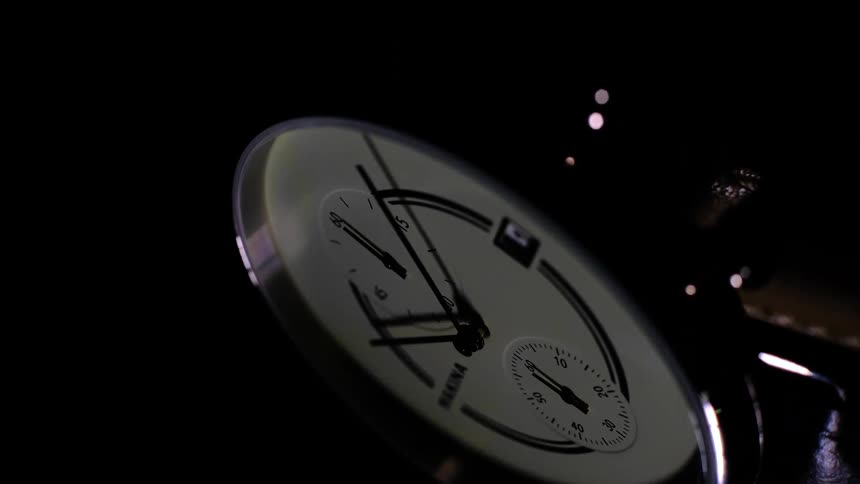 Close up of the dial of an analog wristwatch under moving lights and shadows