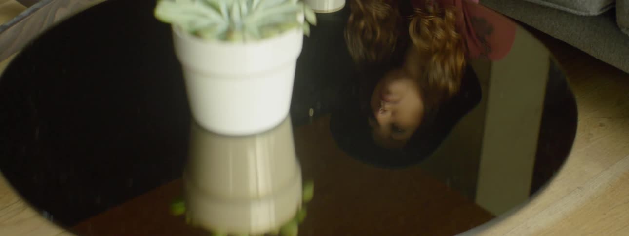 A plant is sitting on a table with a woman's reflection on it