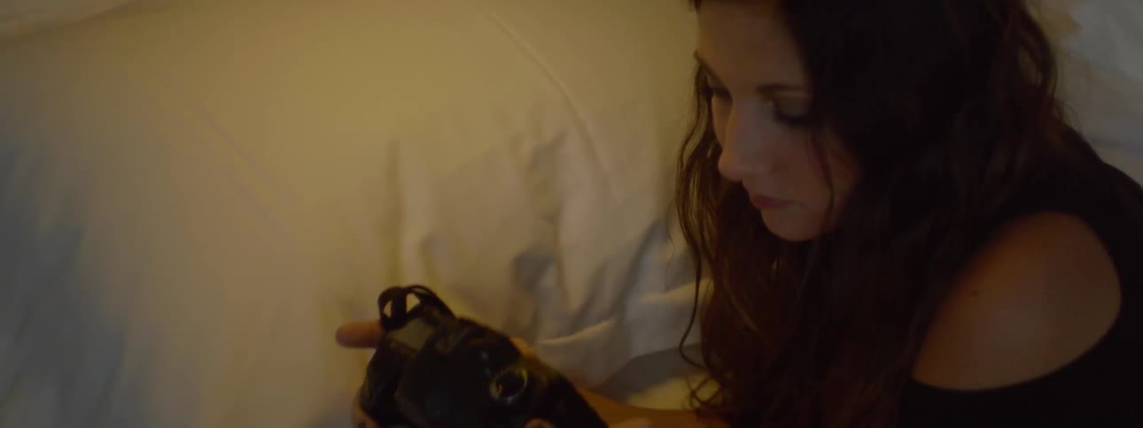A woman views images on a camera while lying on a bed