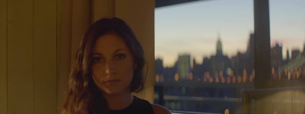 A woman is sitting near a window at sunset