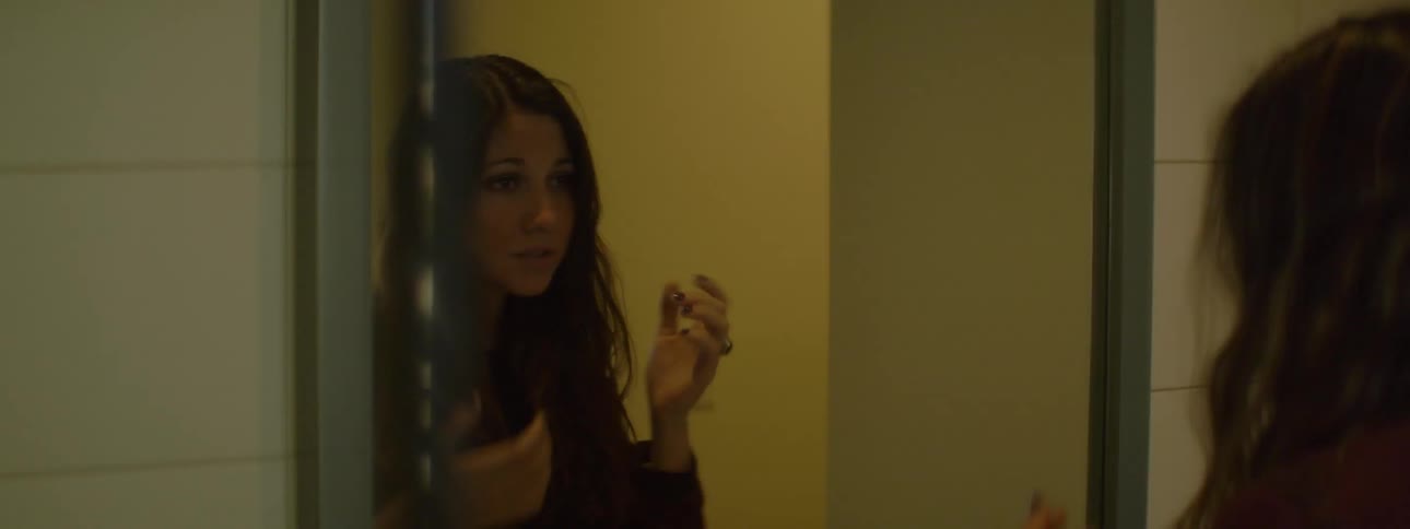 A dark haired woman fixes her hair in the mirror