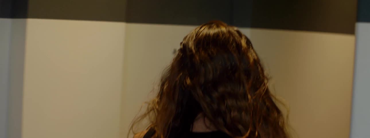A brown haired woman walks down the hall into a building