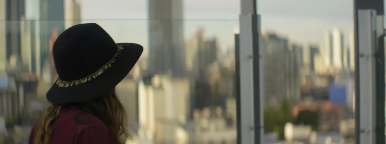 Woman in hat stares out a window at the city view