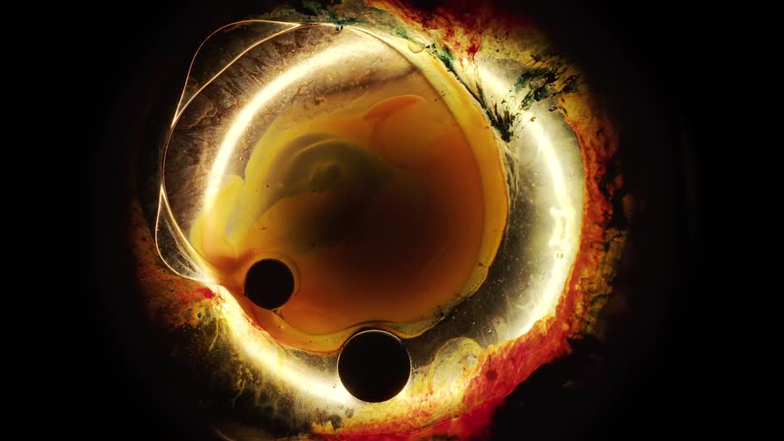 Black particles in liquid shift and slide on a rotating colorful glowing circle