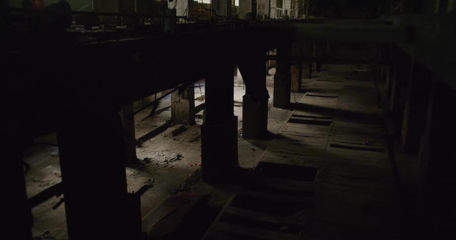 Woman wearing coat walks through dark shadowy abandoned warehouse