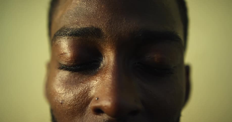 A man staring and closing his eyes with a wall in the background