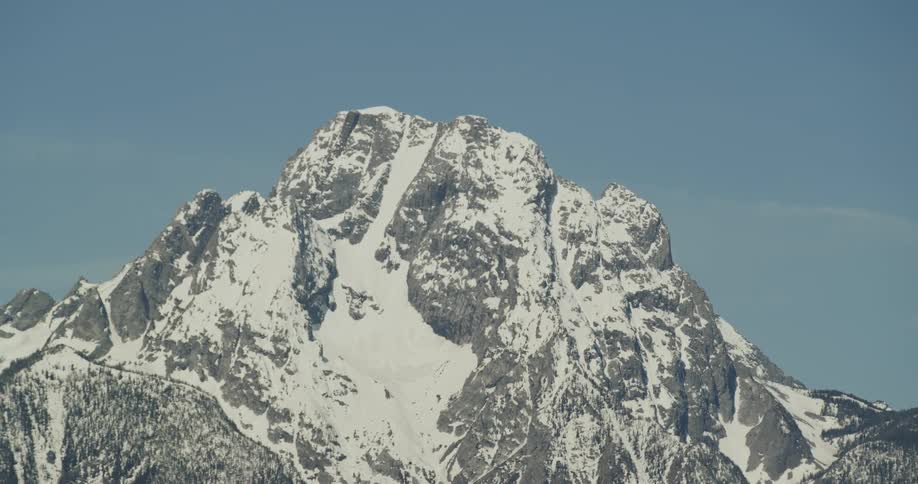 The top of a mountain peak partially covered in snow on a sunny day