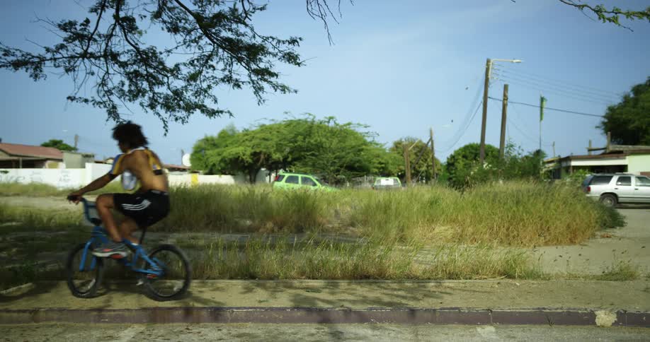 A young man is sitting on a bicycle on a neighborhood sidewalk then rides off