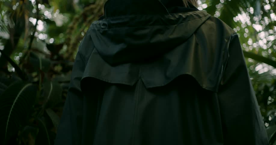 Young blonde woman wearing a raincoat walking through the jungle