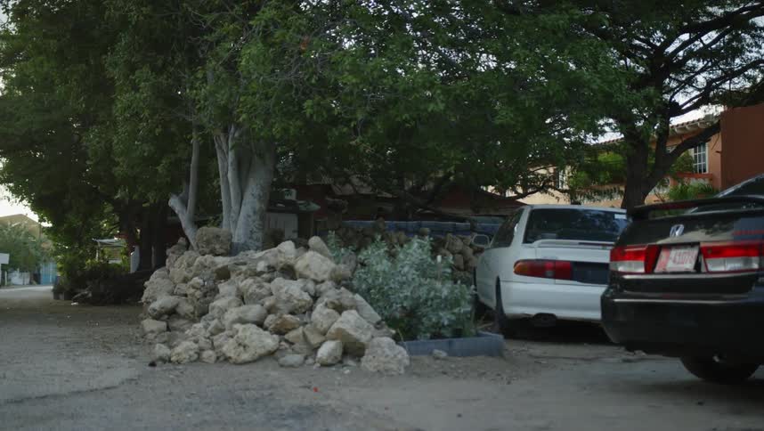 Cars sit in apartment building parking lot near a pile of concrete rubble