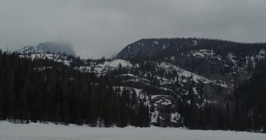 A snow covered ground with trees with a hill fog the sky and clouds in the background