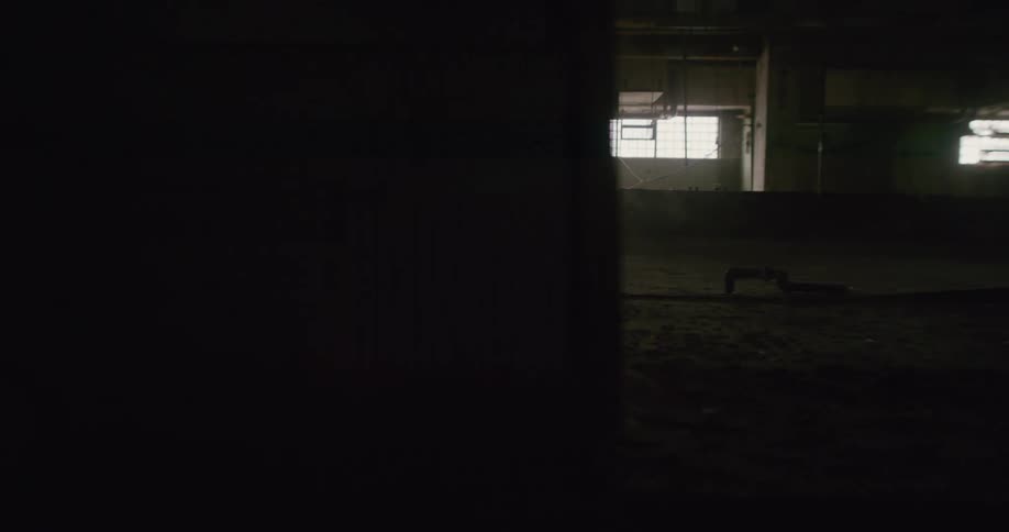 A person wearing a raincoat is walking through a dark abandoned building